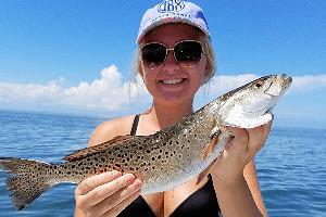 Lady beach angler holding a prized speckled trout she caught.